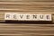 REVENUE word written on wood block at wooden background.