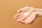 Revitalizing hand cream for recovery. Young woman applying moisturizing lotion. Copy space, close up, beige background.