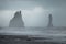 Reynisfjara beach in Iceland with big basalt pillars climbing from water and rocky beach. Cold windi place at the beach with big