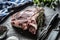 Rib eye steak with bone on butcher board with herbs salt pepper fork and knife