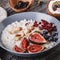 Rice coconut porridge with figs, berries, nuts, dried apricots and coconut milk in plate on rustic wooden background.