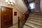 A rich and beautiful staircase with wrought iron railings and a wooden handrail leads to a landing with two wooden doors