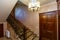 A rich and beautiful staircase with wrought iron railings and a wooden handrail leads to a landing with two wooden doors