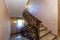 A rich and beautiful staircase with wrought iron railings and a wooden handrail leads to a landing with two wooden doors