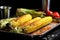 rich golden charred corn on the cob on a shiny metal tray