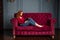 Rich young redhead woman reading a book on red velvet sofa