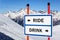 Ride or drink dilemma ski sign with arrows showing opposite directions against snowy mountain peak and blue sky winter scenic