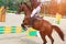 Rider on a chestnut horse jumps over a barrier in jumping competition