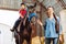 Riding teacher leading horse with blonde-haired beaming girl