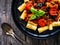 Rigatoni with delicious stew - aubergine with tomatoes and black olives on wooden table