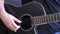 Right hand of a caucasian man playing a black acoustic guitar with fingerstyle