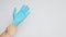 Right hand is pulling left hand wearing blue latex gloves on white background