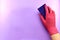 The right hand in a rubber glove with a washing cellulose sponge, a porous surface, on a purple background.