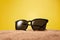 Rimmed sun glasses is on sand on yellow background.