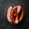 Rings of traditional smoked sausage in a country style composition. on a black stone background. Top view. Free space for text
