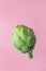 Ripe artichoke floating levitating on pink background. Creative food poster. Mediterranean Spanish cuisine healthy diet