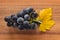 Ripe black grapes with yellow vine leaf on wooden board