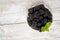 Ripe blackberry with green mint leaves in a white bowl with a gold rim stands on a light wooden background.