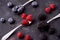 Ripe blueberries, raspberries, blackberries, Mixed berries with three spoons. Various fresh summer berries on dark solid backgroun