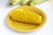 Ripe boiled corn on a yellow plate, raw corn in the background