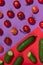 Ripe cherry tomato and green gherkin cucumber with shadow on contrast red and purple background, top view, vertical. Food color.