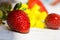 Ripe colorful strawberries on white wood table outdoors in garden yellow spring flowers, bright sunlight