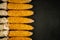 Ripe dried husked corn cobs with braids of leaves lie in a row on the edge of a black concrete surface. top view. artistic autumn