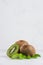 Ripe fleshy green kiwi with juicy slice, young leaves on soft light white table, vertical.