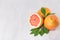 Ripe fresh orange grapefruits and half slice with green leaf on white wood board, top view. Healthy food background.