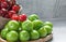 Ripe fresh red cherries and green plums in bamboo bowl on white wooden background