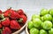 Ripe fresh strawberries and green plums in bamboo bowl on white wooden background