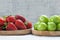 Ripe fresh strawberries and green plums in bamboo bowl on white wooden background