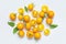 Ripe fresh yellow orange tomatoes with green tails, leaves on light gray background flat lay top view. Cherry tomatoes. Vegetables