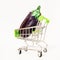 Ripe glossy eggplant lies in a miniature cart on wheels on a white background