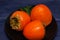 Ripe golden three persimmons on plate, dark background. These sweet and pulpy fruits can be eaten fresh, dried, raw, or