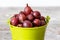 Ripe gooseberries and green leaves in a bucket on a blurred background