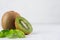 Ripe green kiwi with half cut and juice drop flow down and young leaves closeup on white wood board.