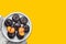 Ripe juicy dark plums cut in half on white plate on yellow background. Summer autumn fruits