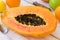 Ripe juicy halved papaya on kitchen table with citrus fruits and apples, knife on plank wood table