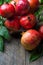 Ripe juicy organic bright red pomegranates in metal wicker basket with branches green leaves on plank barn wood background