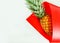 Ripe, juicy pineapple on a light background, wrapped in a red bag. Bright summer image. Free space