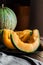 Ripe juicy sliced orange cantaloupe, dark plate, knife, wood kitchen table, rustic interior