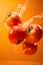 Ripe juicy tomatoes with splashes of drops of water or juice on an orange background, Generative AI