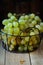 Ripe juicy white Muscat grapes in a wire basket on a wood table, selective focus