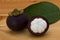 Ripe mangosteens Garcinia mangostana or half mangosteen with green leaves on a wooden table