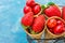 Ripe organic strawberries, glossy sweet cherries in waffle ice cream cones in wire basket, light blue background