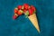 Ripe organic strawberries in waffle ice cream cone, spilling imitation, dark blue background
