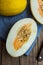 Ripe organic yellow melons, halved and whole on dark plank wood background, pulp and seeds, blue linen napkin, knife