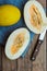 Ripe organic yellow melons, halved and whole on dark plank wood background, pulp and seeds, blue linen napkin, knife, top view