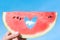 Ripe piece of watermelon with heart shape hole in female hands on the background of the blue sky with little cloud on a hot summer